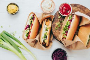 Vegane Hotdogs mit Ketchup, Mayonnaise, Senf, Lauchzwiebeln auf einem Holzbrett