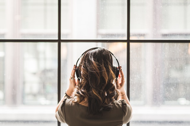 Person mit Kopfhörern, die vor einem Fenster steht als Symbolbild für das Artikelthema vegane Podcasts