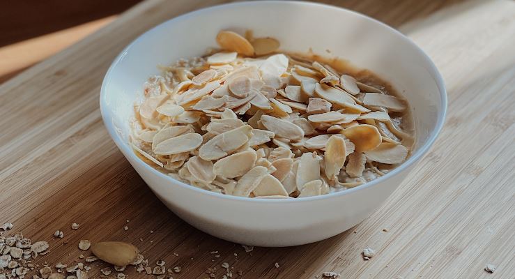Veganes Mandel-Porridge in weißer Schale auf Holzbrett
