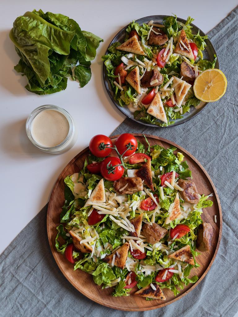 Veganer Caesar Salad auf Holzteller neben Slatkopf und Dressing