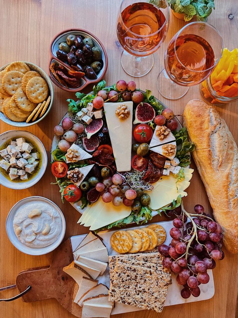 Vegane Käseplatte neben Baguette, Weingläsern und Trauben