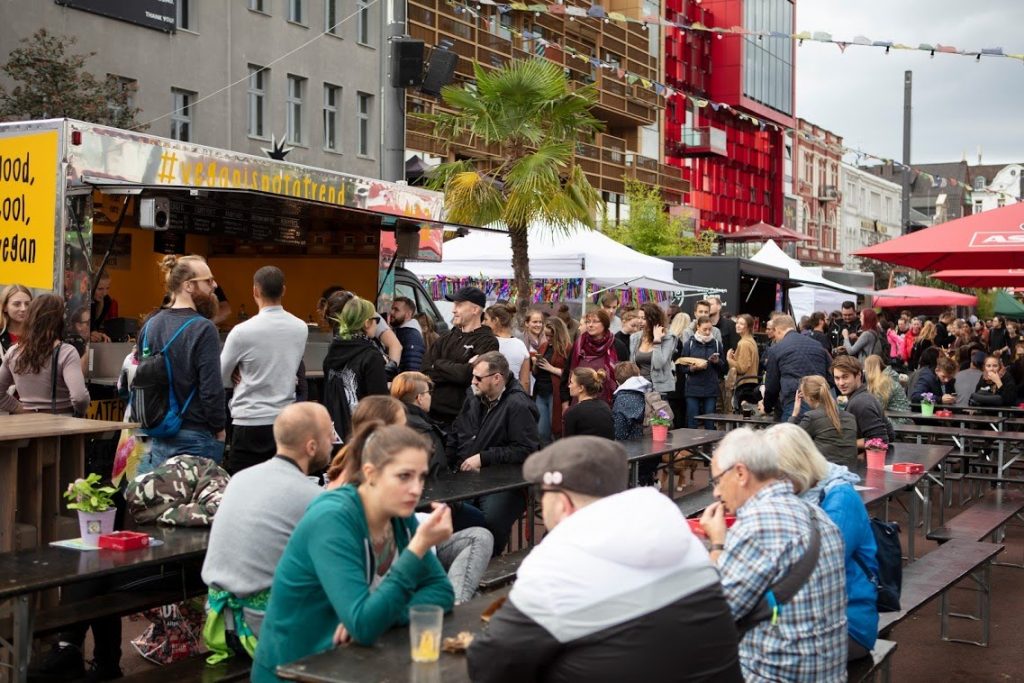 Menschen sitzen auf Bierbänken im Hintergrund ein Foodtruck auf dem Veganen Straßenfest Hamburg