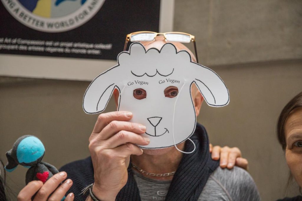 Besucher hät Schafsmaske mit "go vegan" Aufschrift vors Gesicht