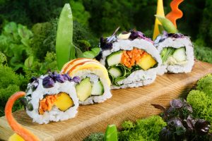 Sushi vegan mit Gemüsefüllung auf Holzbrett mit grünem Hintergrund